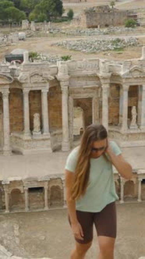 Vertical video. A Young Woman climbs steep steps of the ancient amphitheater, ruins of Hierapolis.