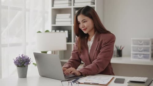 Businesswoman in brown suit is working on laptop with happy face in office space.