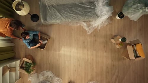 Top View of Living Room Couple Having Fun in New Apartment Man Pushing Woman in Box Through the Room