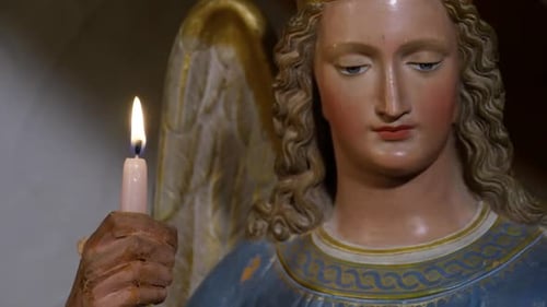 close up of a statue of an angel holding a burning candle in his hand