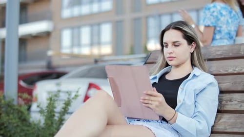 Young Woman Uses Tablet on Bench in City