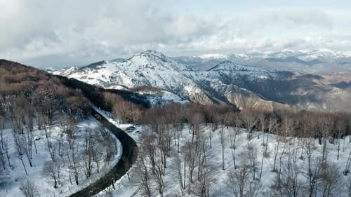 Winter landscape aerial view of a snowy mountain road winding through a forest