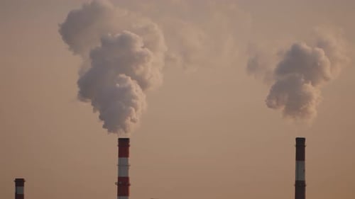 Industrial Chimneys Releasing White Billowing Smoke Against Pale Beige Sky Signaling Environmental