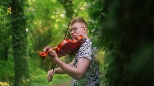 Soulful violinist plays the violin in a dreamy lush green forest, handheld