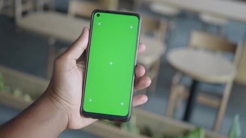 Hand Holding Smartphone with Green Screen in a Cafe Setting