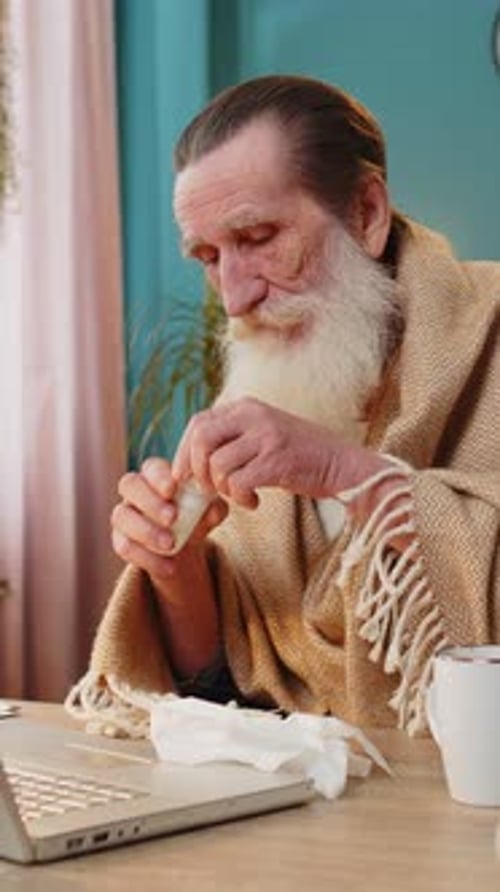 Sick Ill Senior Man Suffering From Cold Flu Allergy Blows Sneezes Wipes Snot Works on Laptop at Home