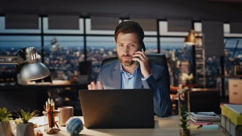 Man Talking on Phone at Desk in Office at Night