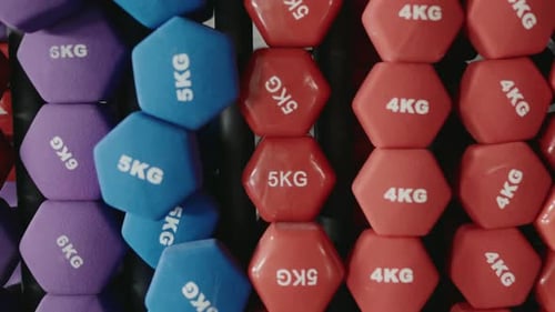 Colorful Dumbbells Weighing 4Kg and 5Kg Organized on a Rack at the Gym
