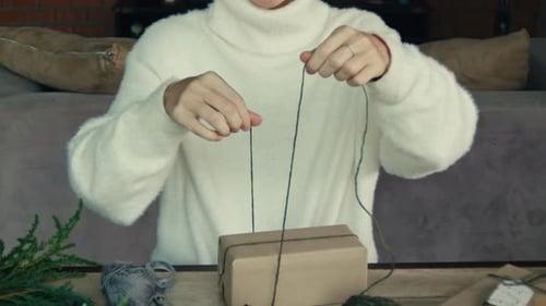 Woman Wrapping Christmas Gift with String Indoors