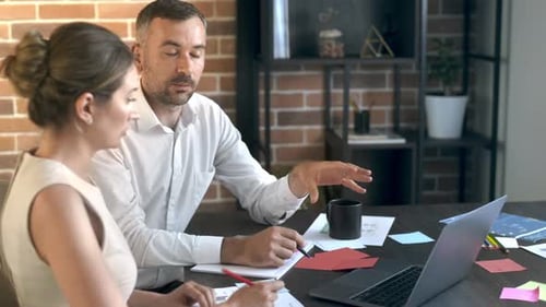 Une femme et un homme qui travaillent et discutent au bureau. Gadgets et documents contenant des informations