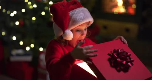 Excited Child Opening Christmas Gift by Fireplace
