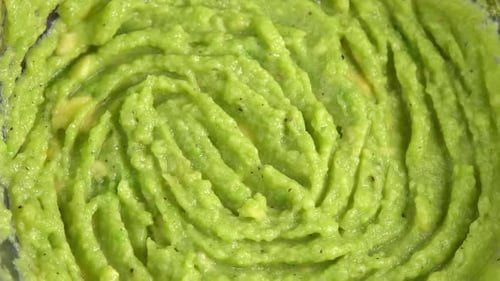 Fresh guacamole dip rotating in glass bowl close up background. Cooking healthy food. Making
