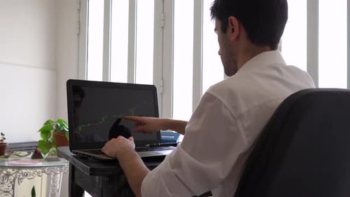 Jovem investidor analisa o movimento do mercado financeiro de ações em um laptop mostrando uma vela otimista