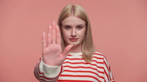 Frau macht Stop-Geste mit offener Hand auf rosafarbenem Hintergrund
