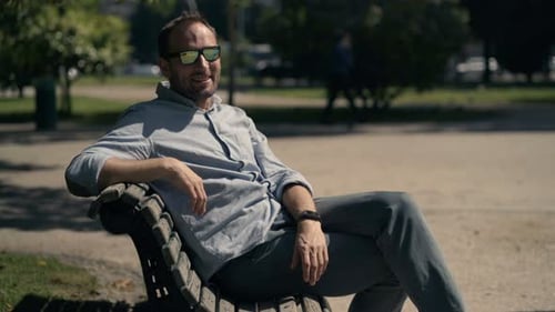 Portrait Of Young, Happy Man Sitting On Bench In City Park