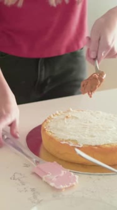 Vidéo verticale : Placer le gâteau sur le comptoir, elle glace et étale du chocolat pour décorer, dessus rose