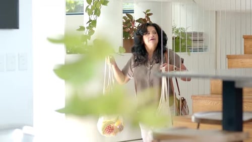 Mujer adulta madura que viene de tiendas y entra en una casa luminosa con bolsas de malla, bolsa de cuero ajustable