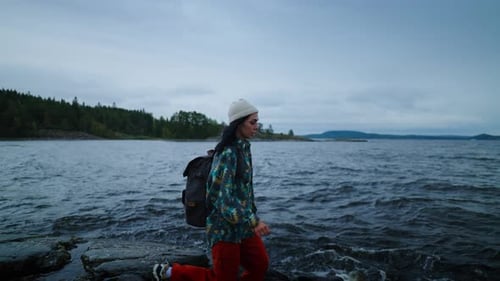 Active Pastime In Weekend Woman With Backpack Walking On Stone Shore Of Beautiful Lake