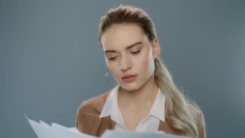 Thoughtful businesswoman looks at documents in studio against grey background