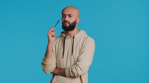 Young Man Thinking with Pen on Blue Background