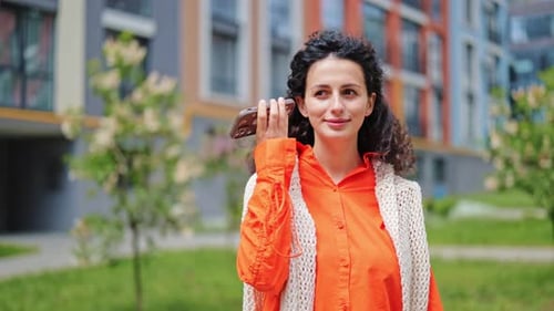 Cheerful Woman Using Phone and Voice Assistant in Modern Apartment Complex Courtyard