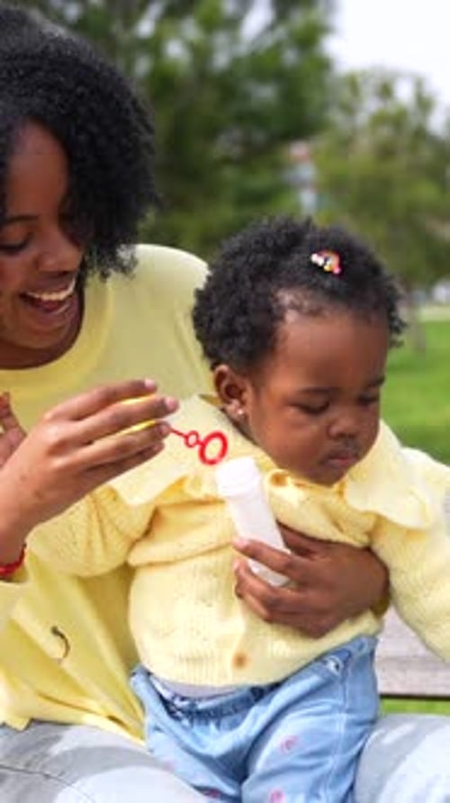 African Woman and Daughter Playing with Soap Bubbles in a Park