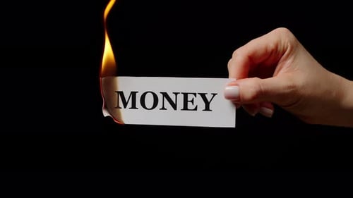 Human Hand Holding Word Money on Burning Paper in Studio