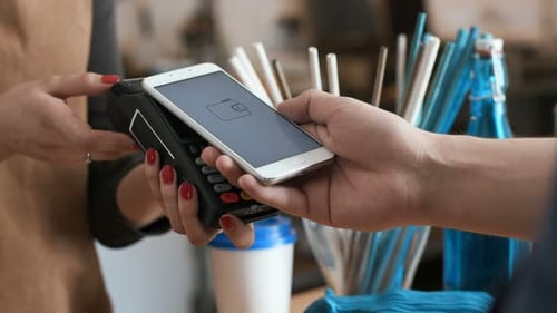 Young woman working at restaurant counter as man pays with nfc cellphone