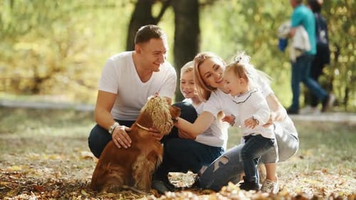 Cheerful young family have a rest in autumn park together and petting dog