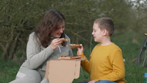 Mother and Son Have Picnic with Pizza in Park Slow Motion