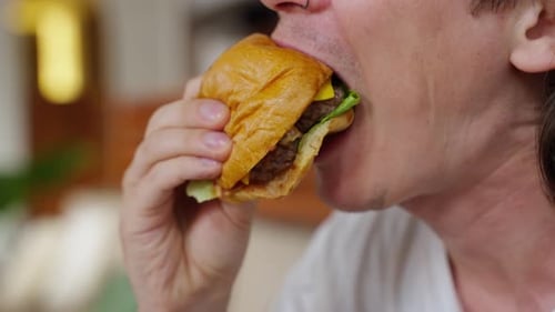 Young Adult Eating Cheeseburger in a Close-Up Shot