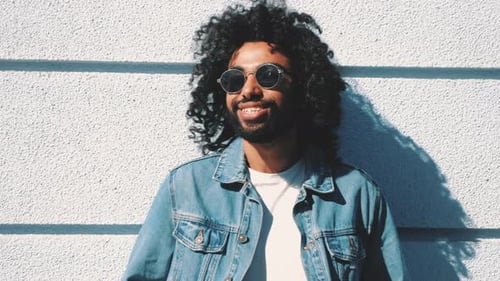 Man with Curly Hair Leans Against Wall in Sunlight