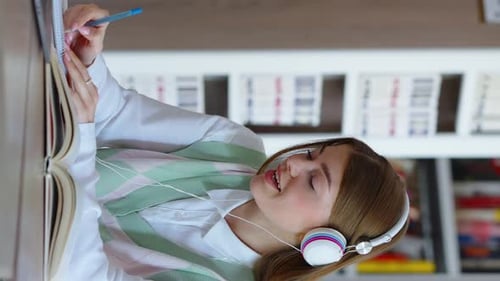 Student mit vertikalem Bildschirm, der in der Bibliothek studiert und Musik hört