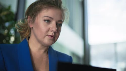Young Female Employee Works at a Computer and Makes Notes in a Notepad While Sitting at a Table in
