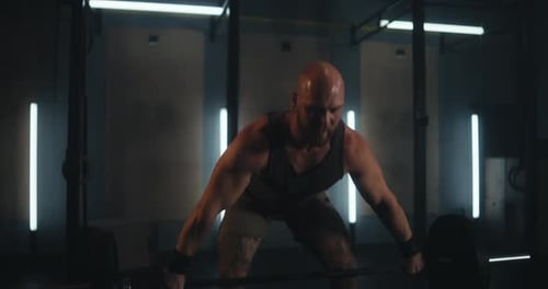 Close Up a Sporty Man with Muscles and a Gray Tshirt Squats and Does Weightlifting with a Barbell in