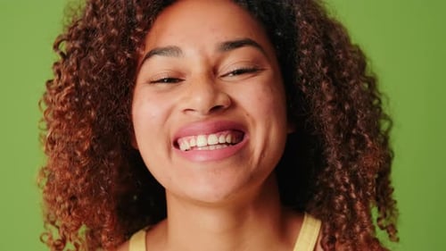 Primer plano de una mujer joven con una amplia sonrisa en el fondo de la pantalla verde, se ríe a carcajadas