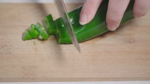 Hand slicing green pepper with kitchen knife on wooden cutting board, Closeup