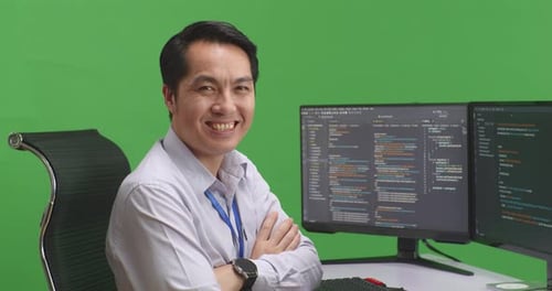 Developer Crossing Arms And Smiling To Camera While Write Code With Multiple Screens In Green Screen