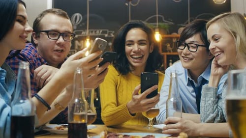 In the Bar/ Restaurant Diverse Group of Friends Have Good Time Sharing Pictures and Whatnot with Th