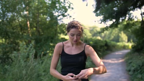 Pretty woman running on a park trail stops to answer a call on her phone. Lady smiling and laughing
