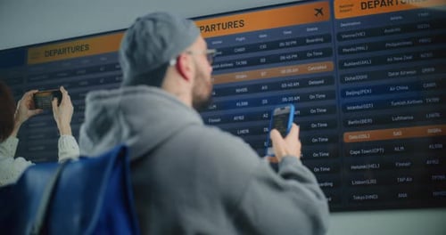 Man Looking for Flight at Arrival and Departure Information Display Using Smartphone