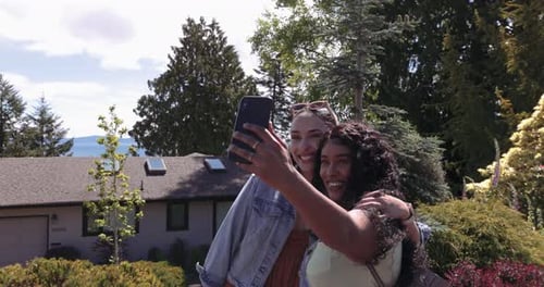 Two Smiling Women Take Selfie Outdoors on Sunny Day