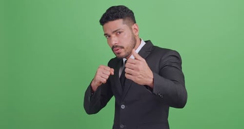 Asian businessman in a black suit is fighting for something. Isolated on green background in studio.