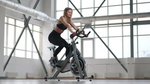 Blonde Woman Exercising on Stationary Bike in Gym
