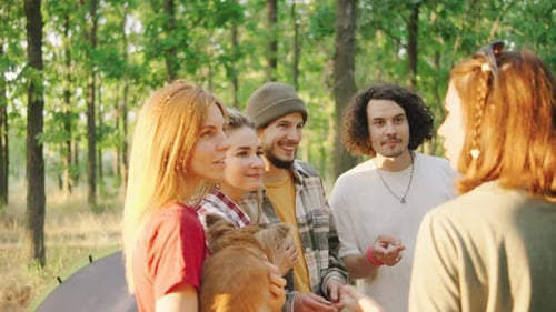 A Group of Friends Tourists Happily Talking and Laugh in the Forest with Tents in the Warm Sun Rays