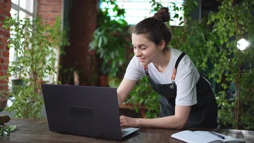 Female Florist Gardener Working in Botanical Store Greenhouse Using Laptop Order Plants