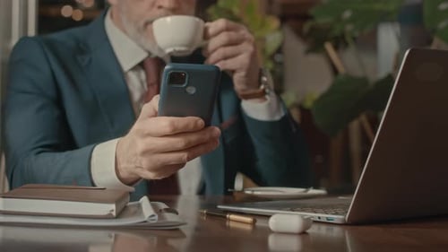 Bearded Businessman Using Smartphone and Drinking Coffee in Cafe