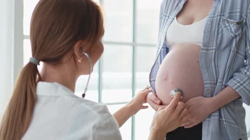врач слушает беременную женщину стетоскопом