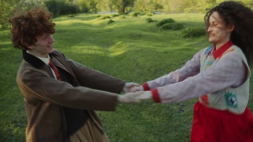 Young Romantic Couple Holding Hands and Spinning on Green Lawn