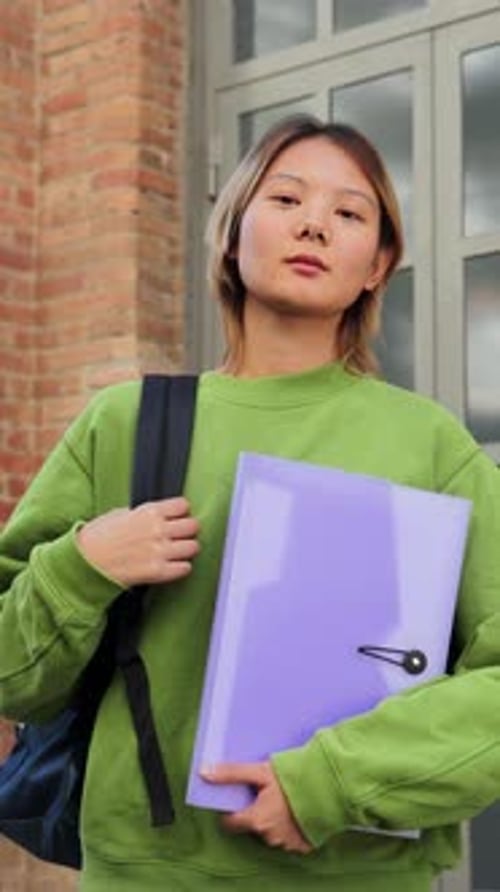 Vertical Asian Teenage Student Looking Serious at Camera Standing on the University Campus Holding a